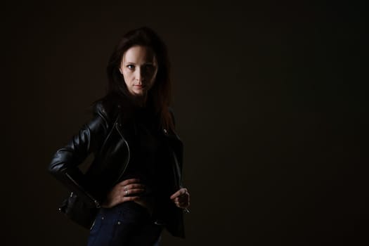 portrait of an attractive young brunette woman in a black leather jacket standing on a black background