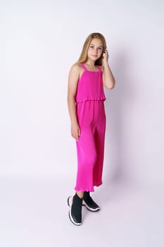 Beautiful girl teenager posing in a pink jumpsuit on a white background. Stylish and youthful bright clothes for a young professional fashion model