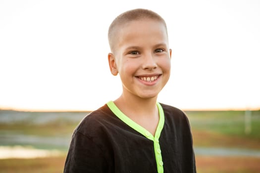 Happy little boy smiling. Guy of caucasian ethnicity in a black t-shirt looking at the camera on nature in summer