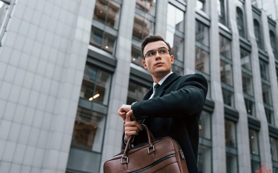 Checking the time. Businessman in black suit and tie is outdoors in the city.