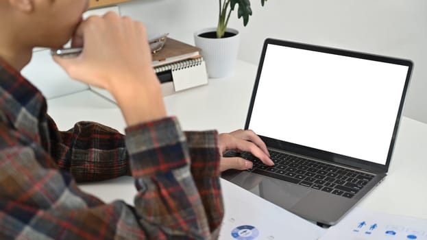 Cropped shot of young hipster male freelancer using laptop computer at white working desk.