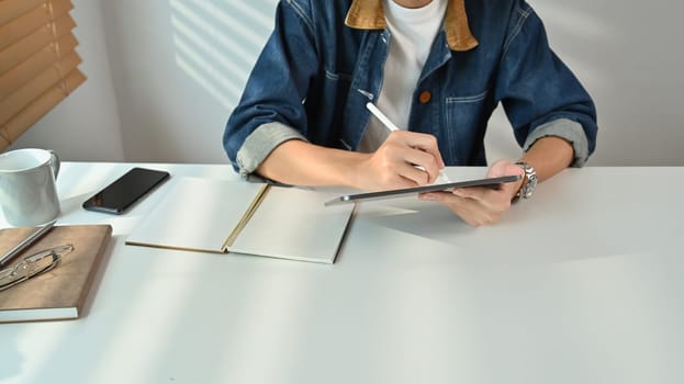 Man freelancer wearing jeans jacket browsing internet or sending email on digital tablet during working at home.