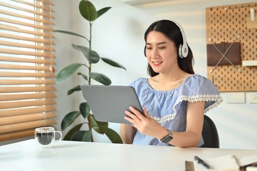 Attractive woman wearing wireless headphone and checking social media or working online on digital tablet.