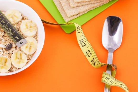 oatmeal with sliced bannana and crispbread lie with spoon and yellow measuring tape on orange background, healthy food and dita concept