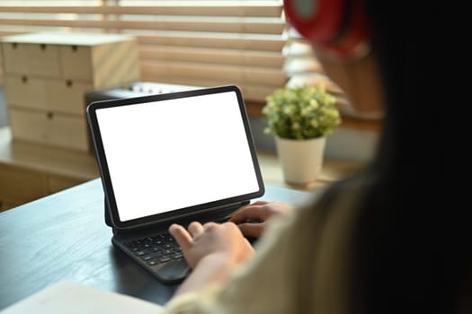 Close up view of student girl wearing headphone typing on keyboard of digital tablet. Online education, e-learning concept.