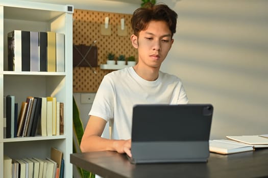 Young asian male looking at digital tablet, working or doing research or preparing for exam online. Education and technology.
