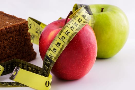 Black sliced bread and green and red apples lie on a white background with a yellow measuring tape, diet concept