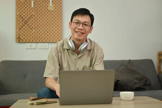 Happy man wearing glasses and headphone watching online education webinar on laptop at home.