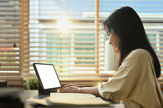 Smiling teenage girl using digital tablet, studying remotely at home. Homeschooling, online education, e-learning concept.