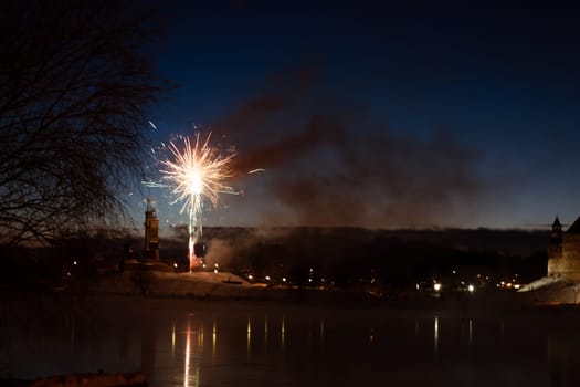 fireworks in the night sky against the backdrop of the city landscape. The sky is hazy, and the lights are reflected in the water