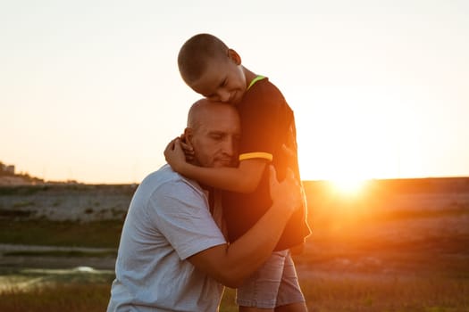 Son and dad standing against the backdrop of a colorful sunset. The relationship between father and son. Family's soulful walk in nature in the rays of the setting sun