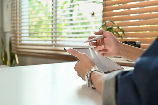 Close up view of man searching information, surfing the internet with digital tablet, sitting working desk in home office.