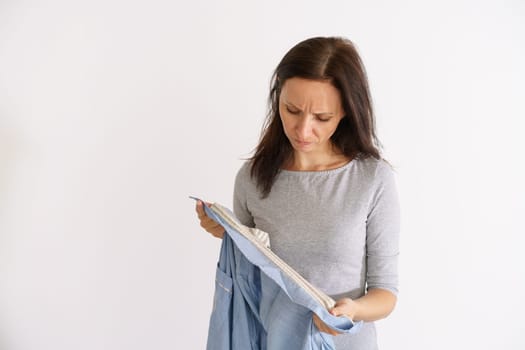 Caucasian woman looking at dirty bad smelling shirt on light background