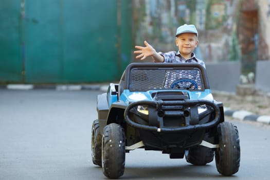 The boy plays, drives a car in the park. A cute little boy of Caucasian appearance in a cap driving a large mechanical toy truck,