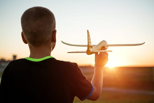 Boy throws a toy airplane in the summer at sunset. A child plays with a toy airplane, dreams of a trip. Son plays by plane in the field at sunset. Have fun and enjoy life