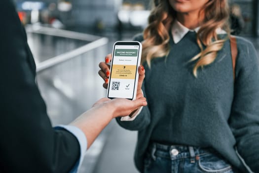 Vaccination certificate in the phone. Young female tourist is in the airport at daytime.