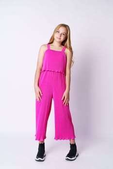 Beautiful girl teenager posing in a pink jumpsuit on a white background. Stylish and youthful bright clothes for a young professional fashion model