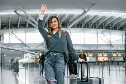 Hello gesture. Young female tourist is in the airport at daytime.