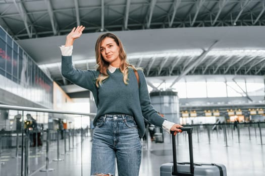 Hello gesture. Young female tourist is in the airport at daytime.