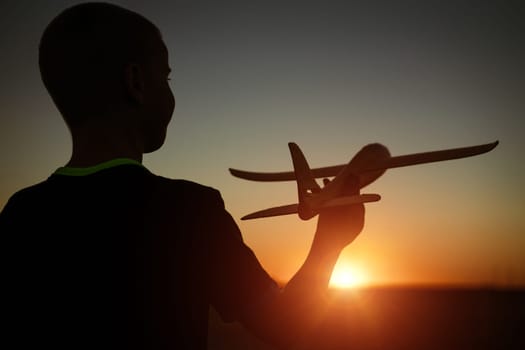 Boy throws a toy airplane in the summer at sunset. A child plays with a toy airplane, dreams of a trip. Son plays by plane in the field at sunset. Have fun and enjoy life