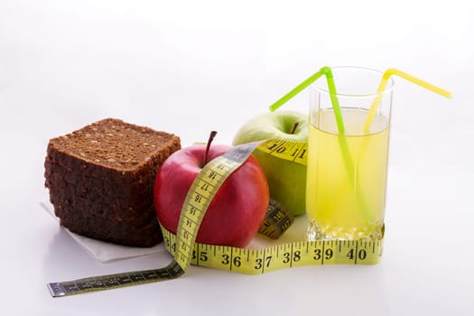 Rye bread with green and red apples and juice in a glass on a white plate with a yellow measuring tape. Diet and healthy food concept