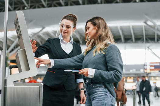 Employee helping to use terminal. Young female tourist is in the airport at daytime.