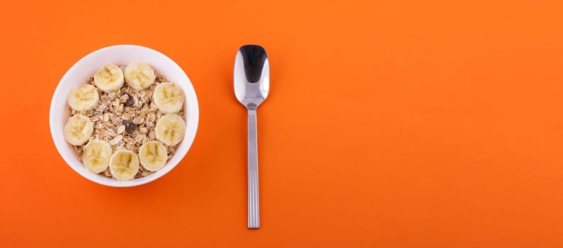 oatmeal in white plate with sliced banana and spoon on orange background, healthy food concept