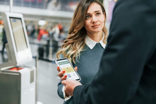 Certificate of vaccination in the phone. Young female tourist is in the airport at daytime.