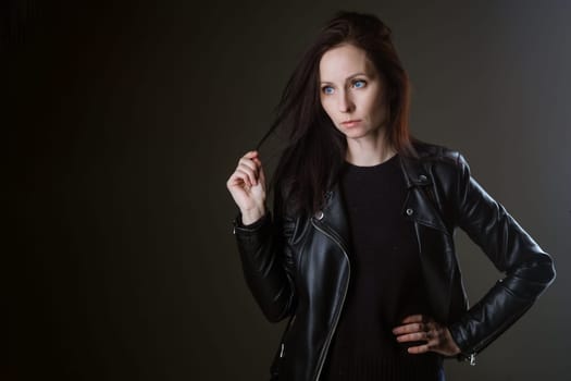 portrait of an attractive young brunette woman in a black leather jacket standing on a black background