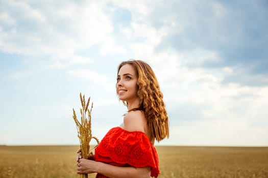 Young beautiful woman in golden wheat field. Happy woman in red dress enjoying life in field. Nature beauty. Outdoor lifestyle. Freedom concept. Summer field. Young beautiful woman golden wheat field