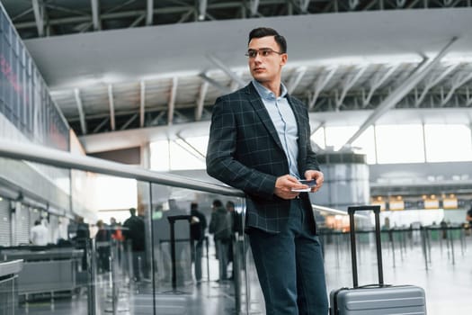 Front view. Young businessman in formal clothes is in the airport at daytime.