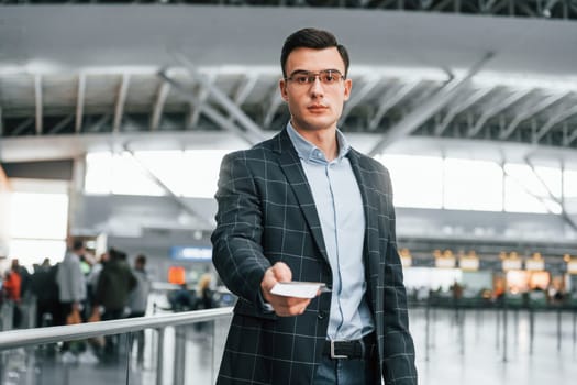 Front view. Young businessman in formal clothes is in the airport at daytime.