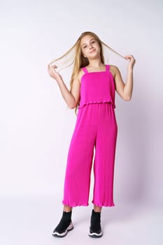 Beautiful girl teenager posing in a pink jumpsuit on a white background. Stylish and youthful bright clothes for a young professional fashion model