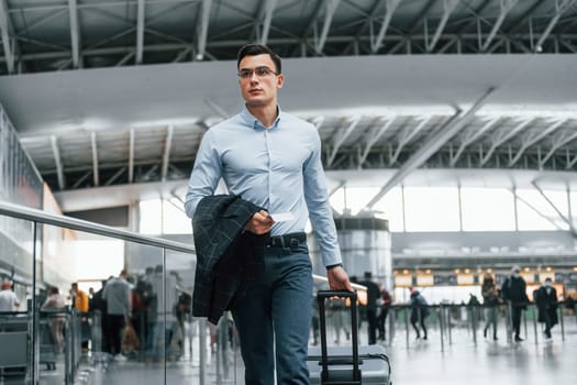 Front view. Young businessman in formal clothes is in the airport at daytime.