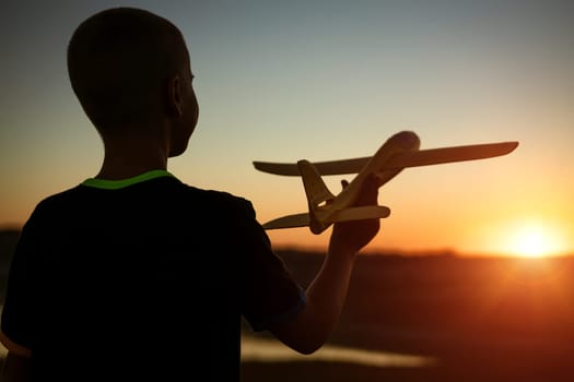 Boy throws a toy airplane in the summer at sunset. A child plays with a toy airplane, dreams of a trip. Son plays by plane in the field at sunset. Have fun and enjoy life