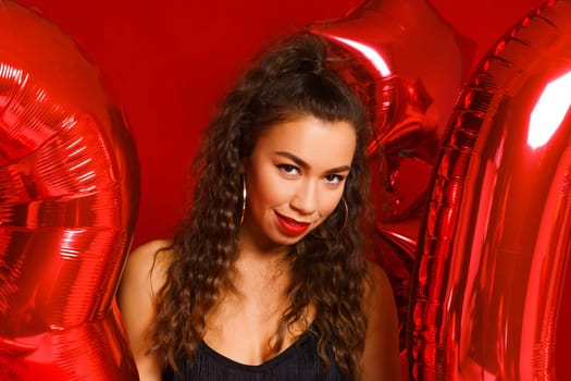 Portrait of happy 30 year old woman on red background with red balloons. A beautiful girl of Caucasian appearance is celebrating her anniversary. Balloons in the form of numbers 30 and stars.