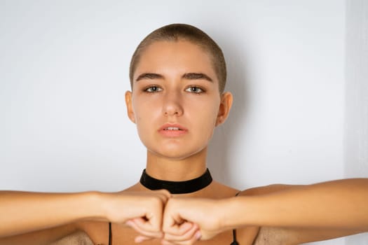 Portrait of a young woman with a short haircut in a black dress with clenched fists on a light background