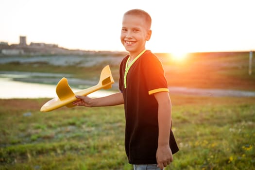 Boy throws a toy airplane in the summer at sunset. A child plays with a toy airplane, dreams of a trip. Son plays by plane in the field at sunset. Have fun and enjoy life