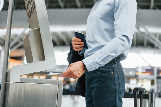 Using terminal. Young businessman in formal clothes is in the airport at daytime.