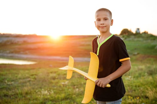 Boy throws a toy airplane in the summer at sunset. A child plays with a toy airplane, dreams of a trip. Son plays by plane in the field at sunset. Have fun and enjoy life