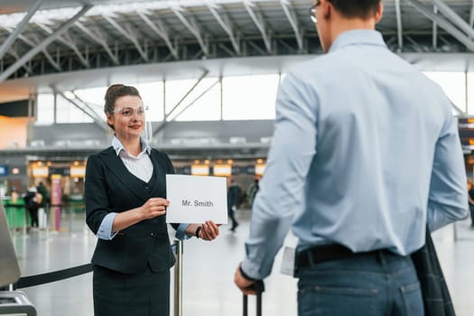 Meet by the woman with text. Young businessman in formal clothes is in the airport at daytime.