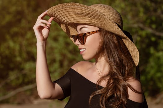 Close-up portrait of a woman in a hat from the sun on a summer sunny day. Beautiful caucasian young woman posing in sunglasses outdoors in the afternoon cute smiling