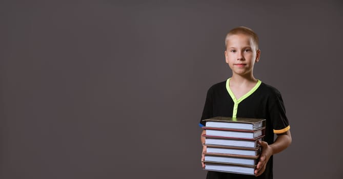 schoolboy boy in black t-shirt holding a stack of books on a gray background