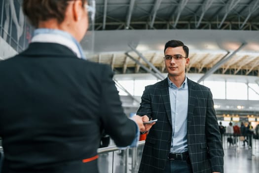 Giving the documents. Young businessman in formal clothes is in the airport at daytime.