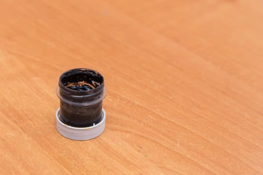 An old open jar of black gouache for painting. Side view of a half-empty can of gouache paint. There is empty copy space.