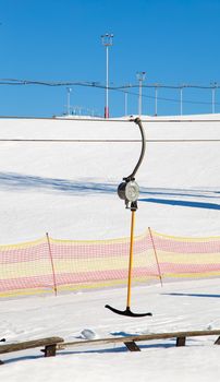 Cable car lift in a ski resort and poles with artificial lighting. Mountain slope for skiing and snowboarding. Against the background of the blue sky. Ski tours on a sunny day.