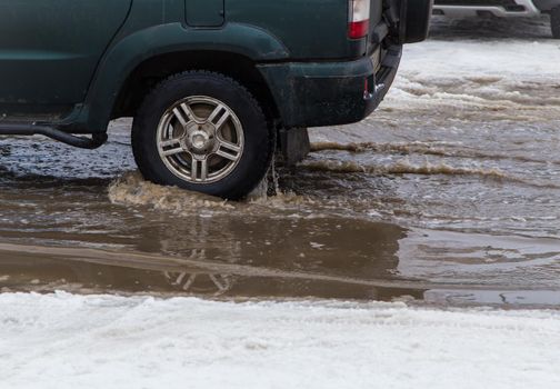 The wheel of a car driving through a deep puddle of melted snow. Abnormal weather concept. There is copy space. The New Year and Christmas celebrations are over. Remains of last year's snow.