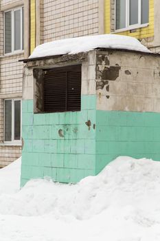 Above ground ventilation shaft with black grating. Air hood for air conditioning in a snowdrift. Against the background of a residential brick house with plastic windows.