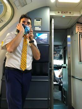 Catania Airport - May, 27: The flight attendant or steward wearing the anti virus protection mask talking on the microphone of the Intercom during a Ryanair flight on May 27, 2021