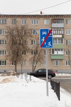 A road sign on the street indicating the end of the residential area. Against the background of a road and a residential building. It's winter in the city, white snow lies on the street.